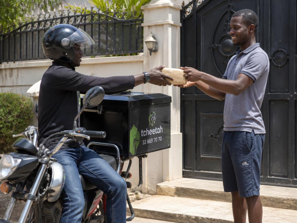 Livreur à moto remettant la clé USB du Coran à un client devant sa maison au Sénégal